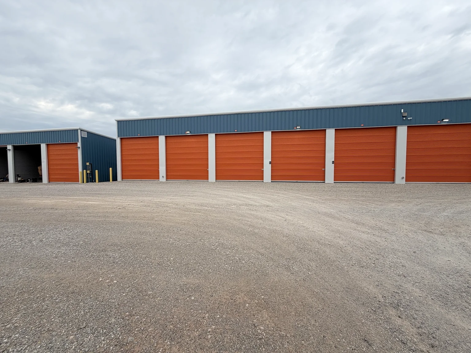 Wide front elevation of a completed blue metal storage building with orange doors