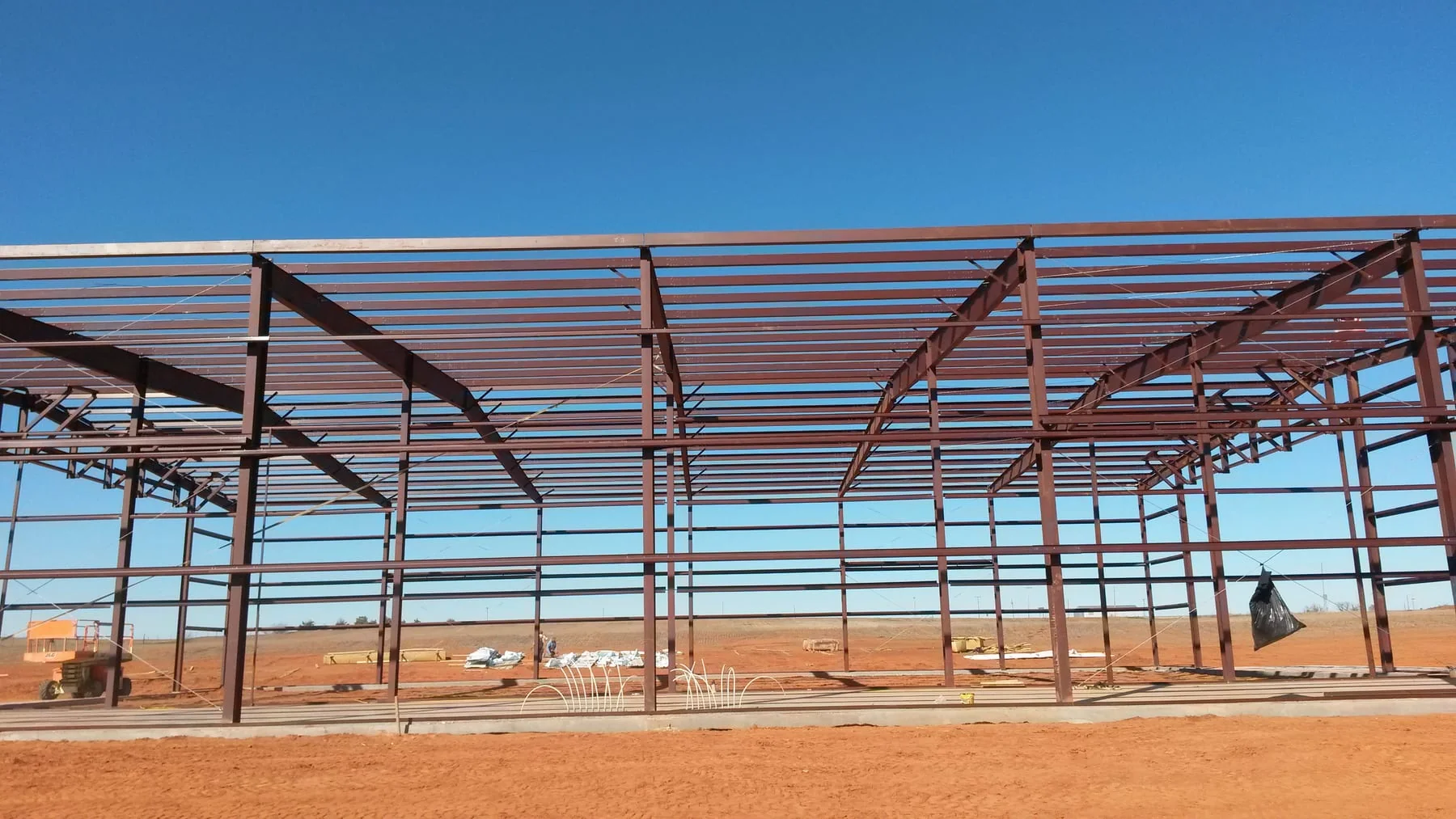 Side view of a red steel building frame under a clear blue sky