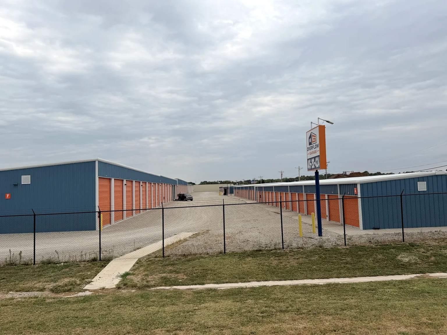 Wide view of blue metal self-storage buildings with orange roll-up doors at Overflow Garage Norman South