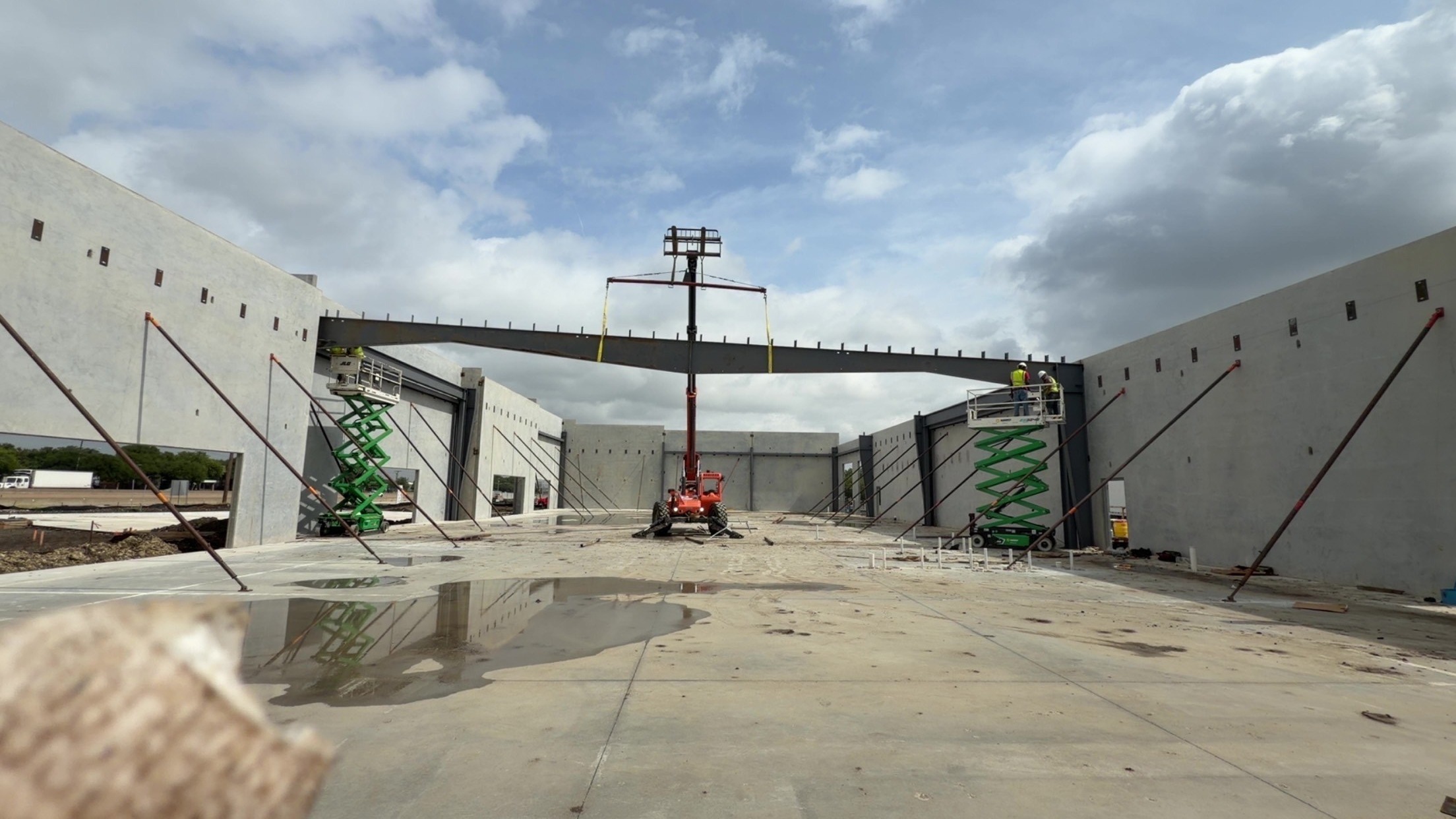 Lifts positioned beneath a long steel beam between concrete wall panels