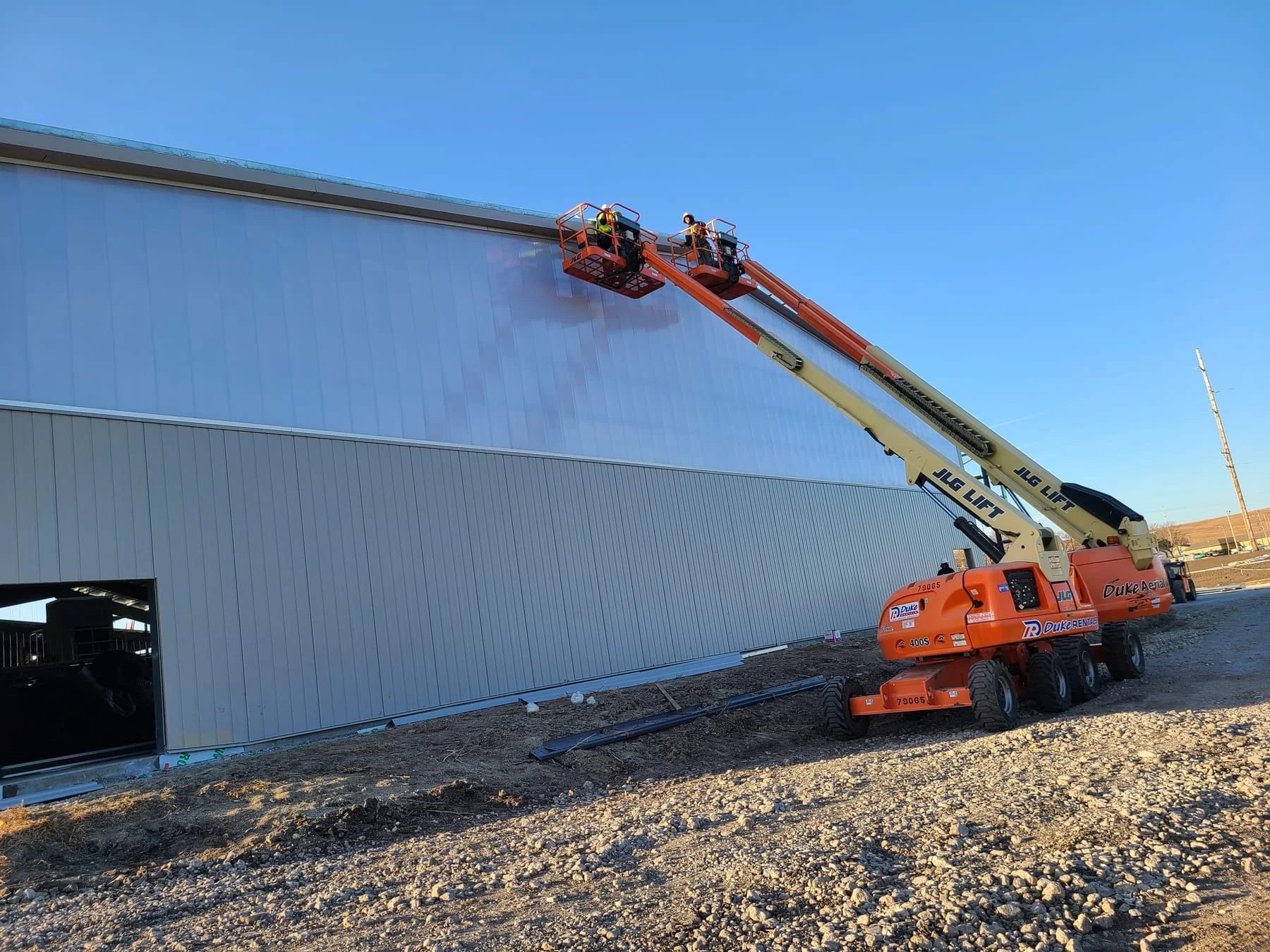 Workers on raised boom lifts installing light metal wall panels