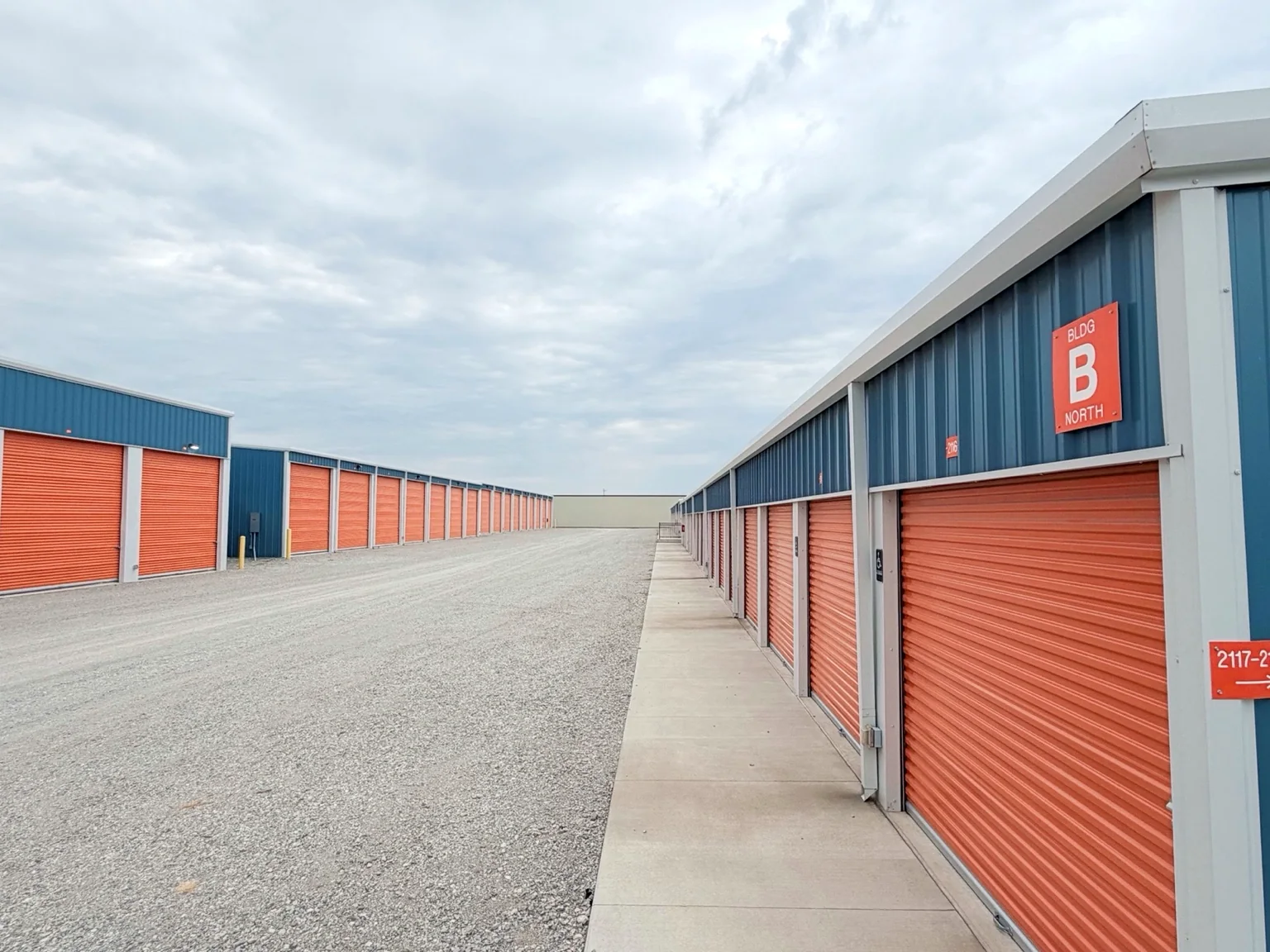 Drive aisle between completed blue metal storage buildings with orange roll-up doors
