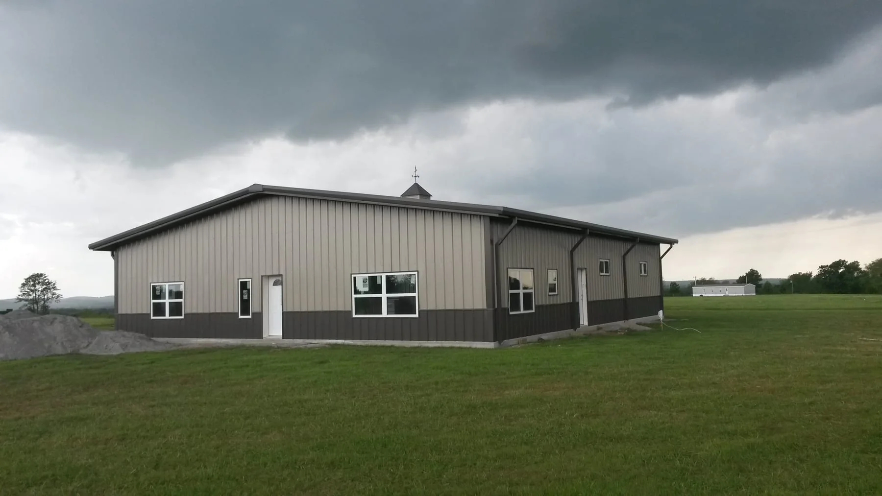 Finished gray metal building with white doors and windows beneath dark clouds