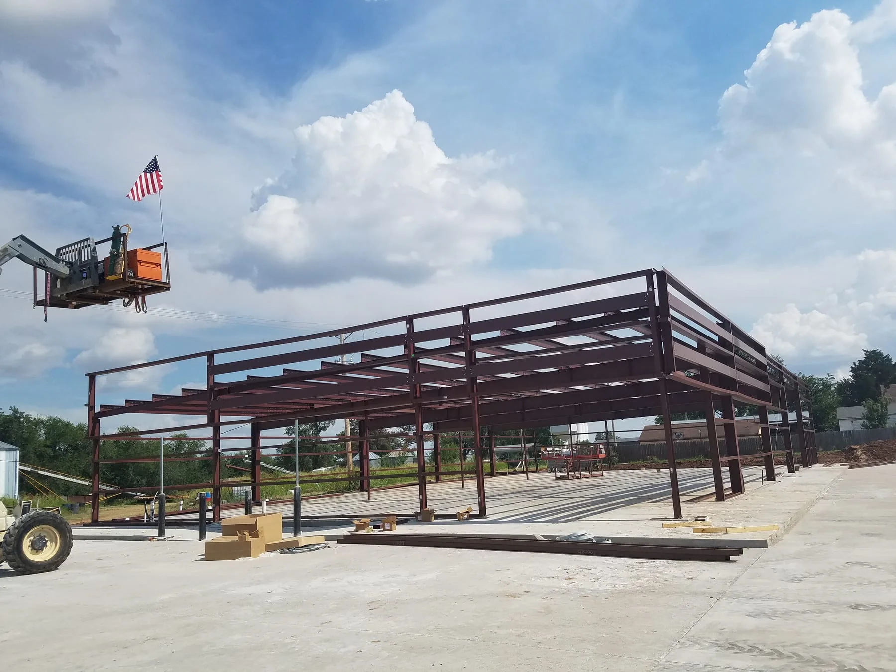 Red steel building frame on a concrete slab with a raised work platform nearby