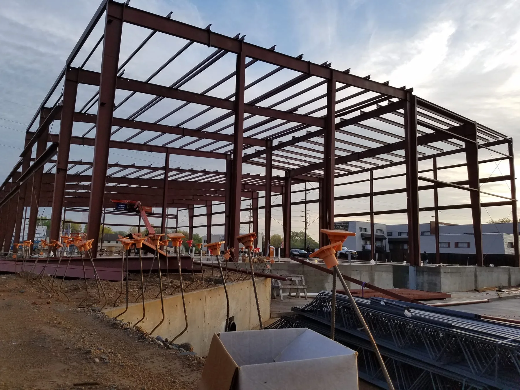 Wide red steel building frame with construction materials in the foreground