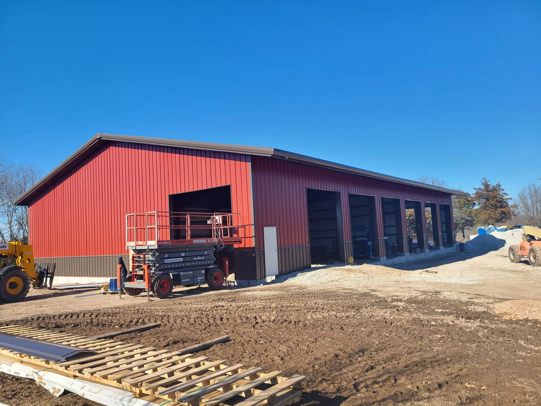 Red metal building with open bays and construction lifts outside