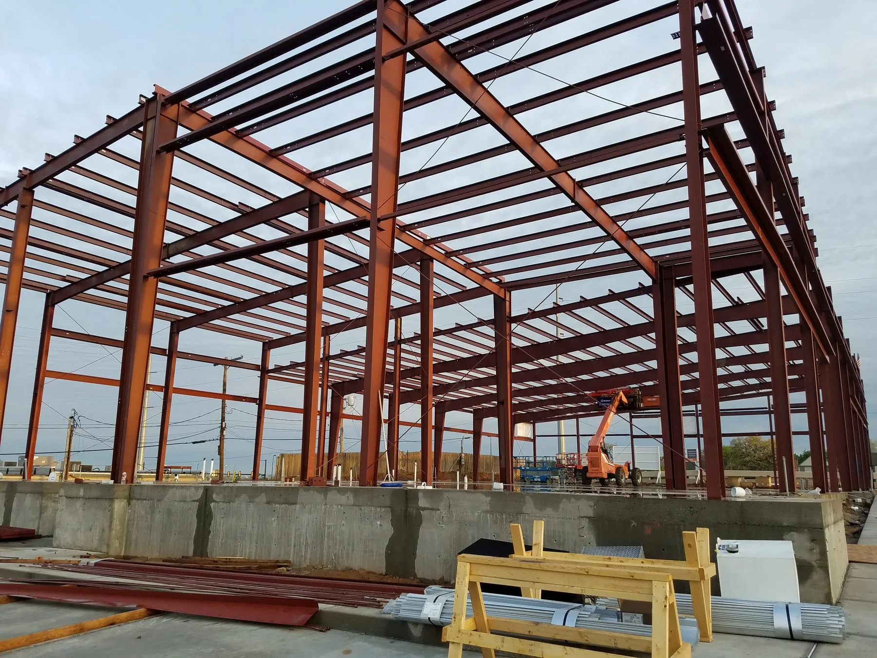 Tall red steel building frame viewed above a concrete foundation wall