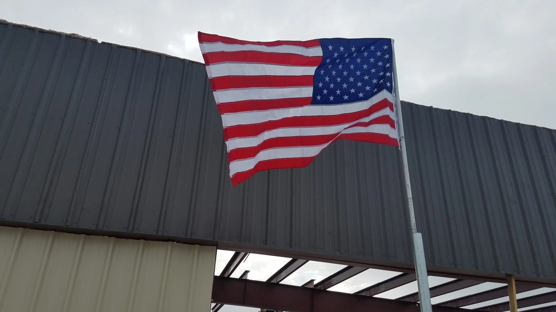 American flag flying in front of dark metal wall panels and exposed steel framing