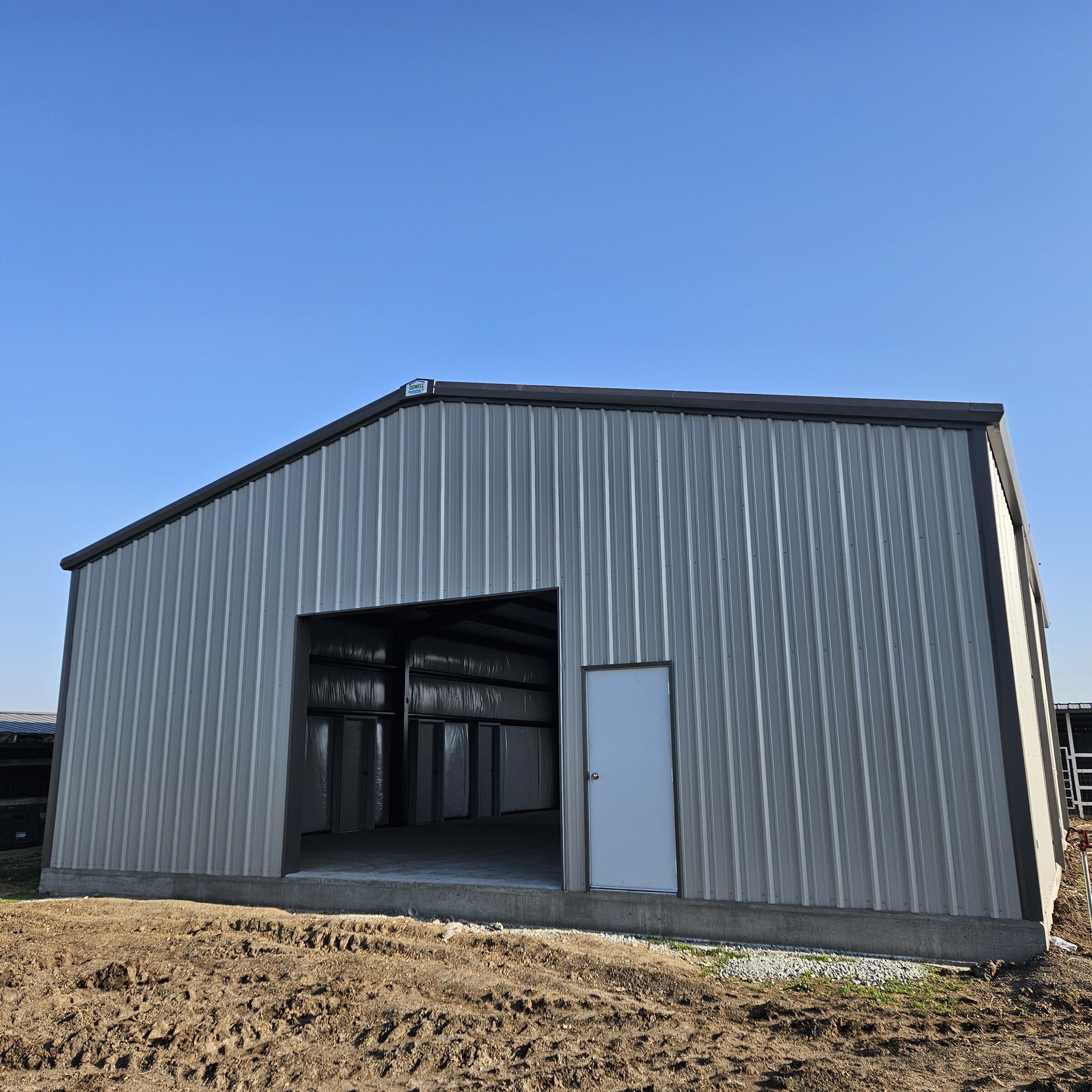 Completed gray metal building shell with an open bay and walk door