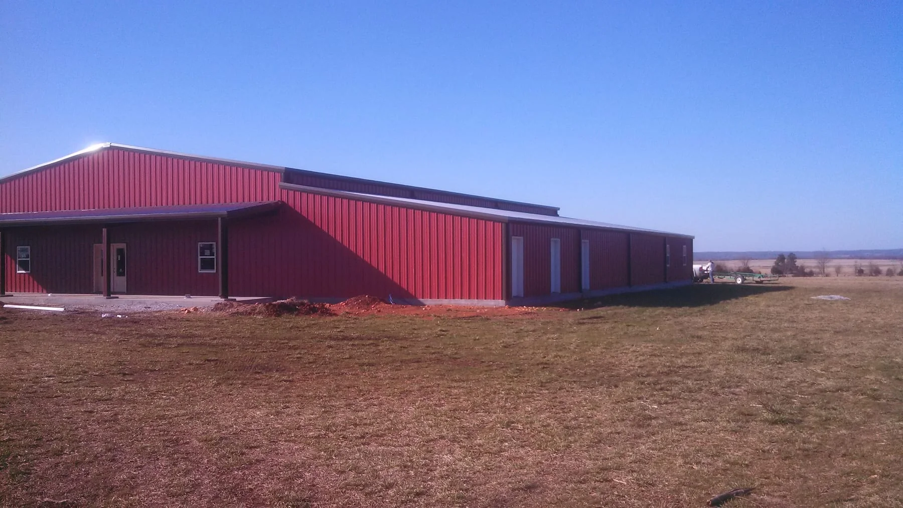 Side view of a red metal building with a covered entrance and several doors