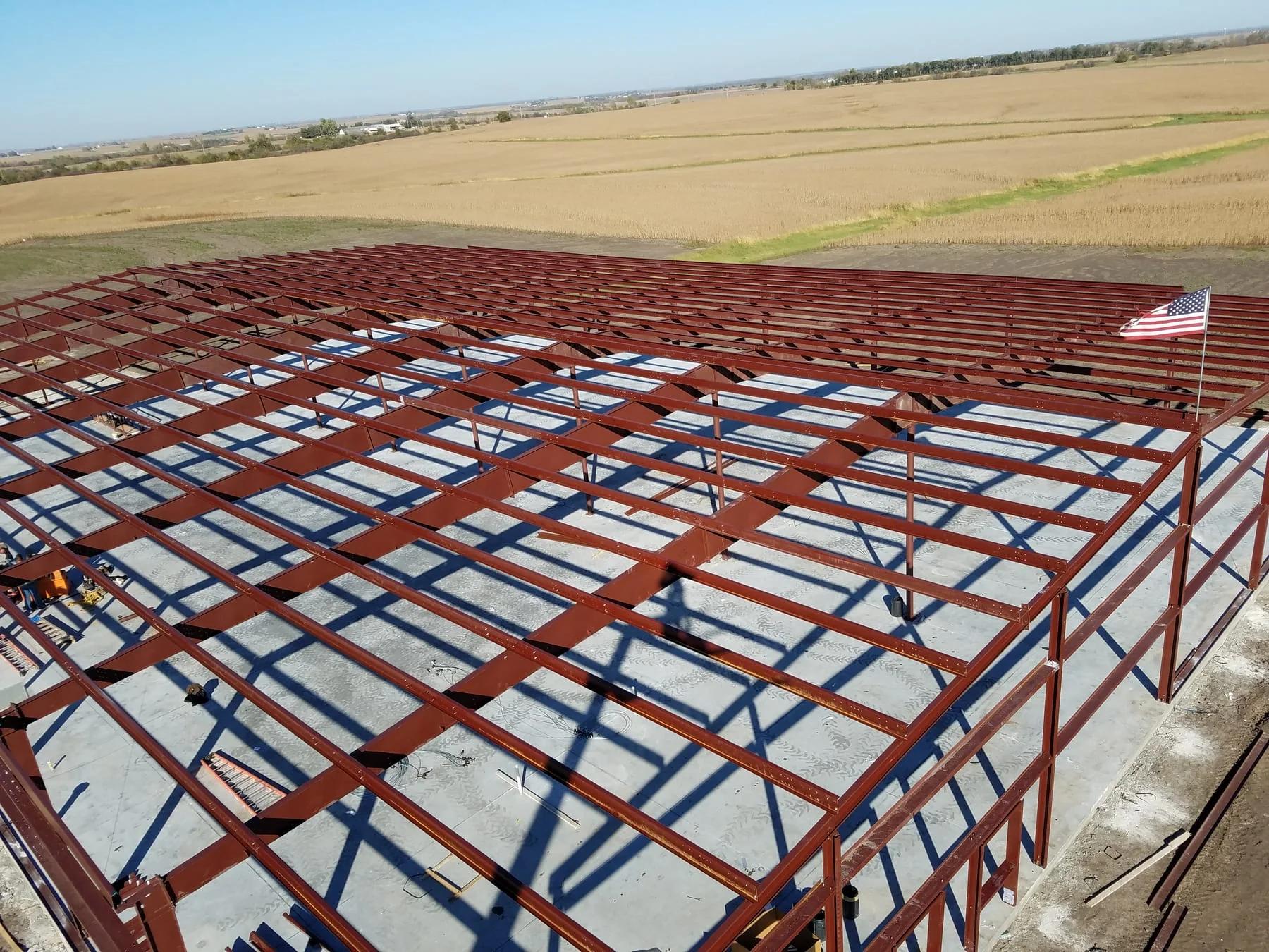 Elevated view across red steel roof framing and the concrete floor below