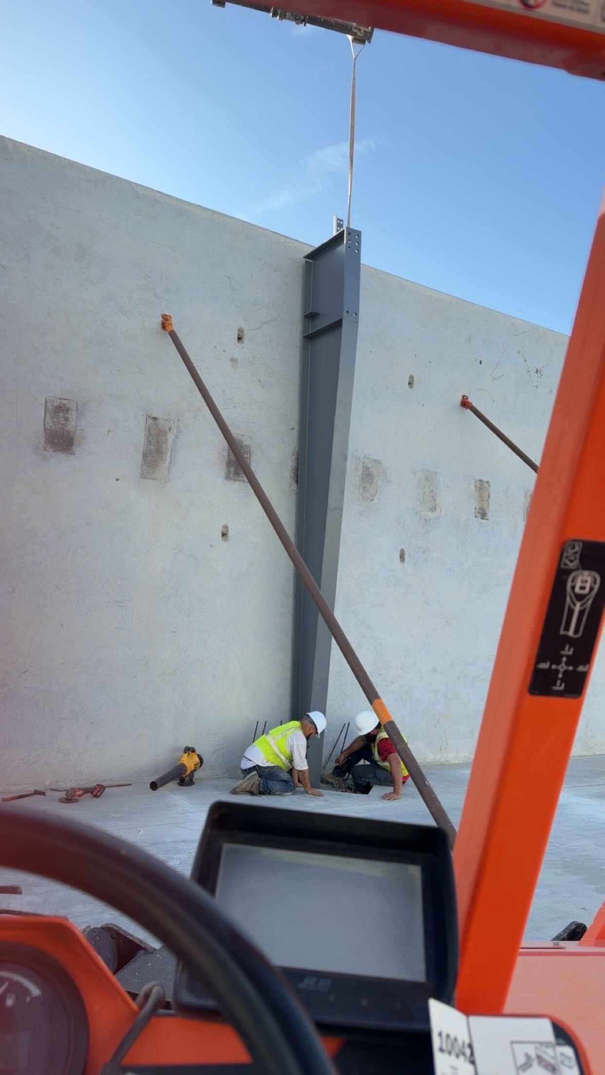Workers positioning a steel column beside concrete wall panels