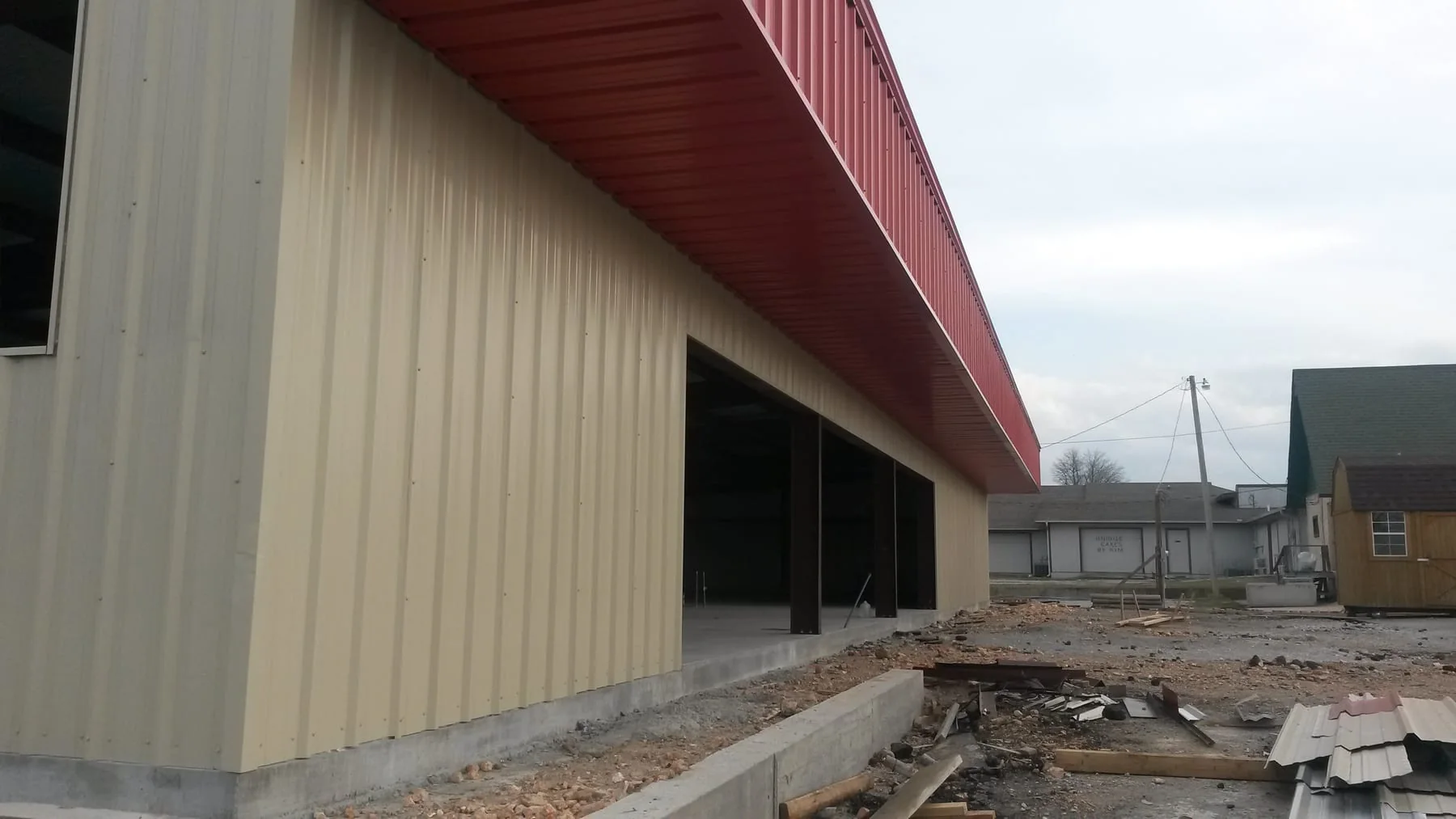Close view of tan metal wall panels, a red canopy and open building bays