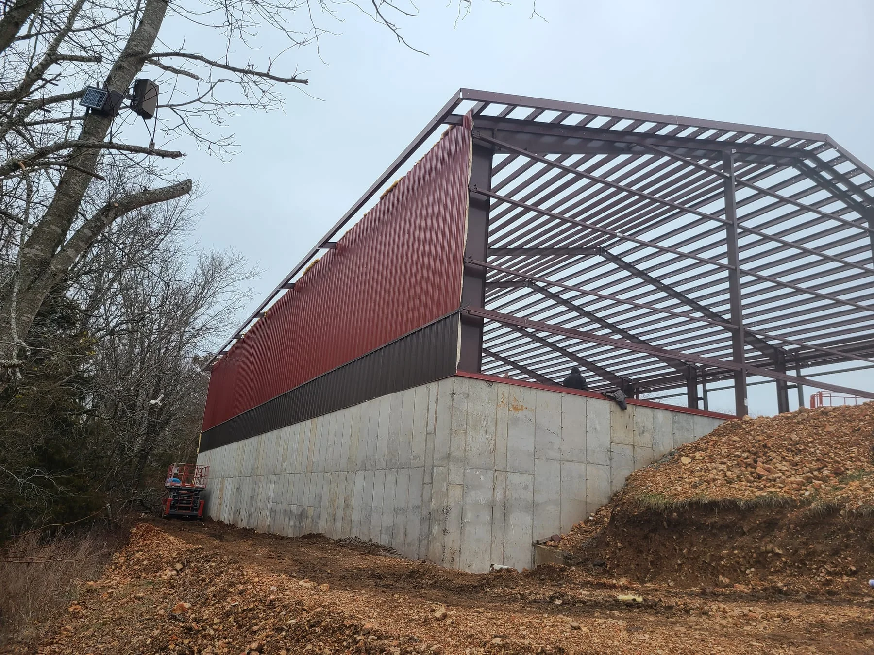 Red steel building frame with partial wall panels above a concrete foundation