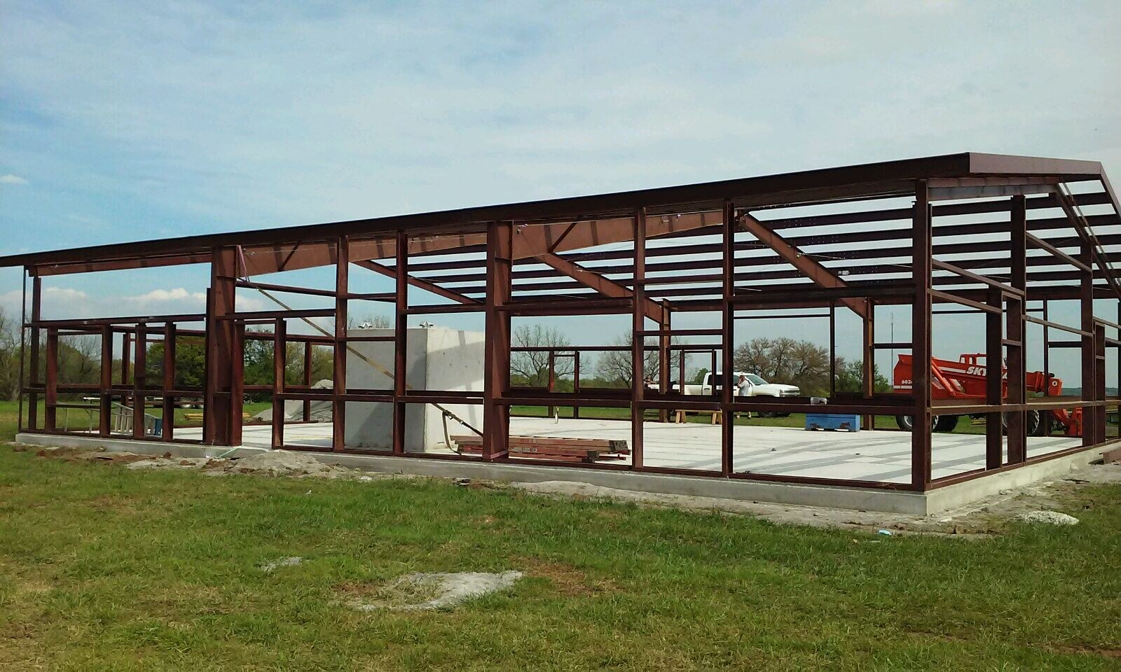 Wide view of a red-iron steel building frame on a concrete foundation