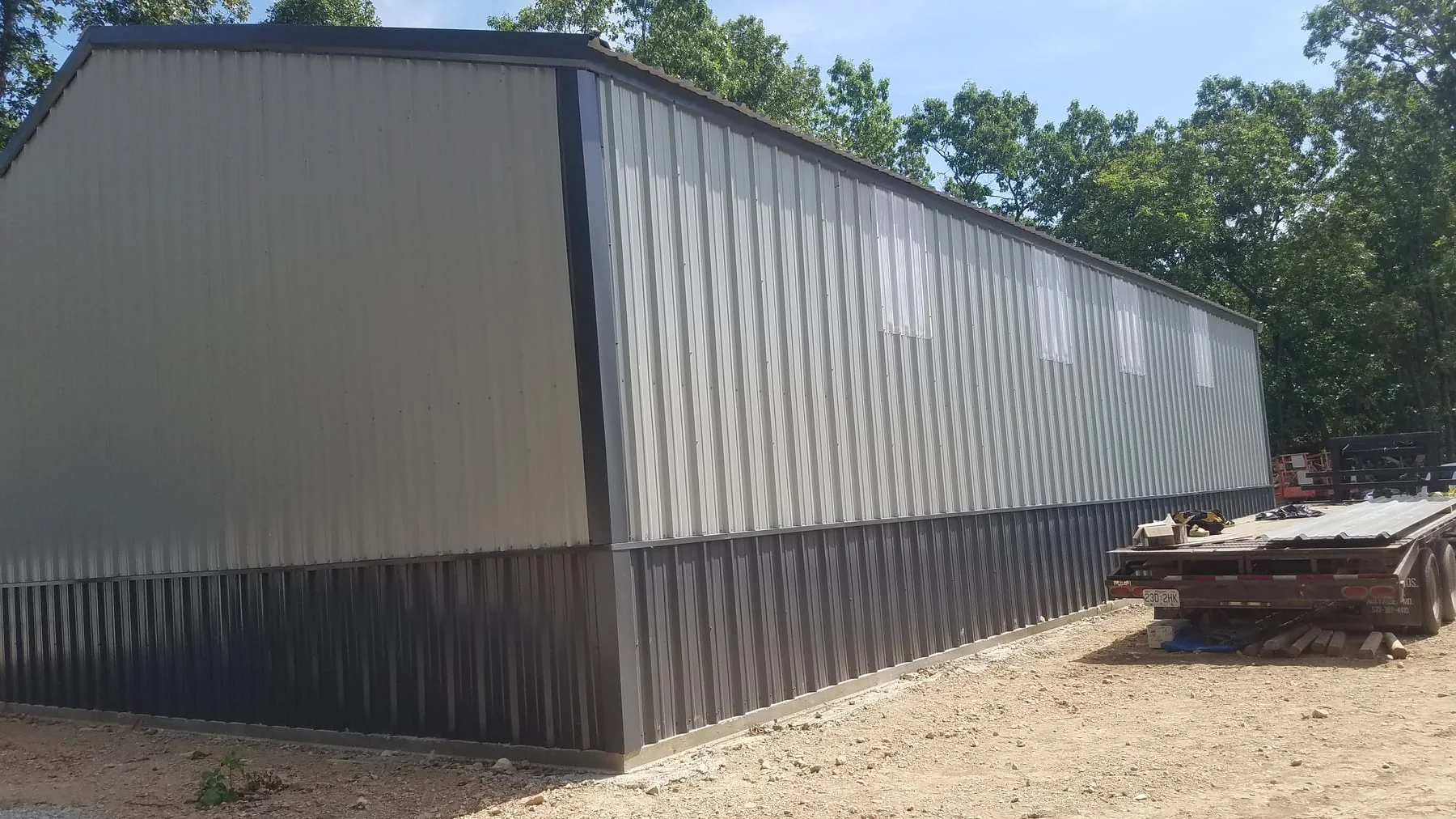 Light metal-sided building with a dark lower wall band beside construction materials