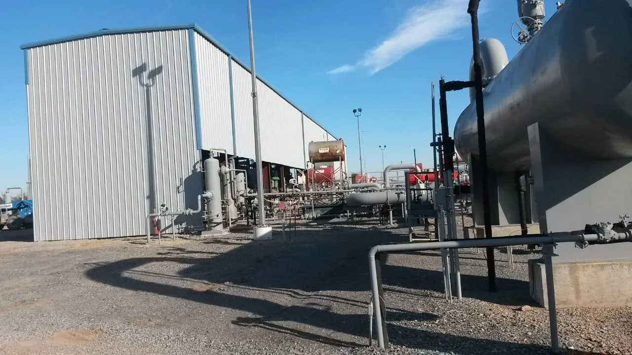 Metal-sided industrial enclosure beside tanks, piping and equipment
