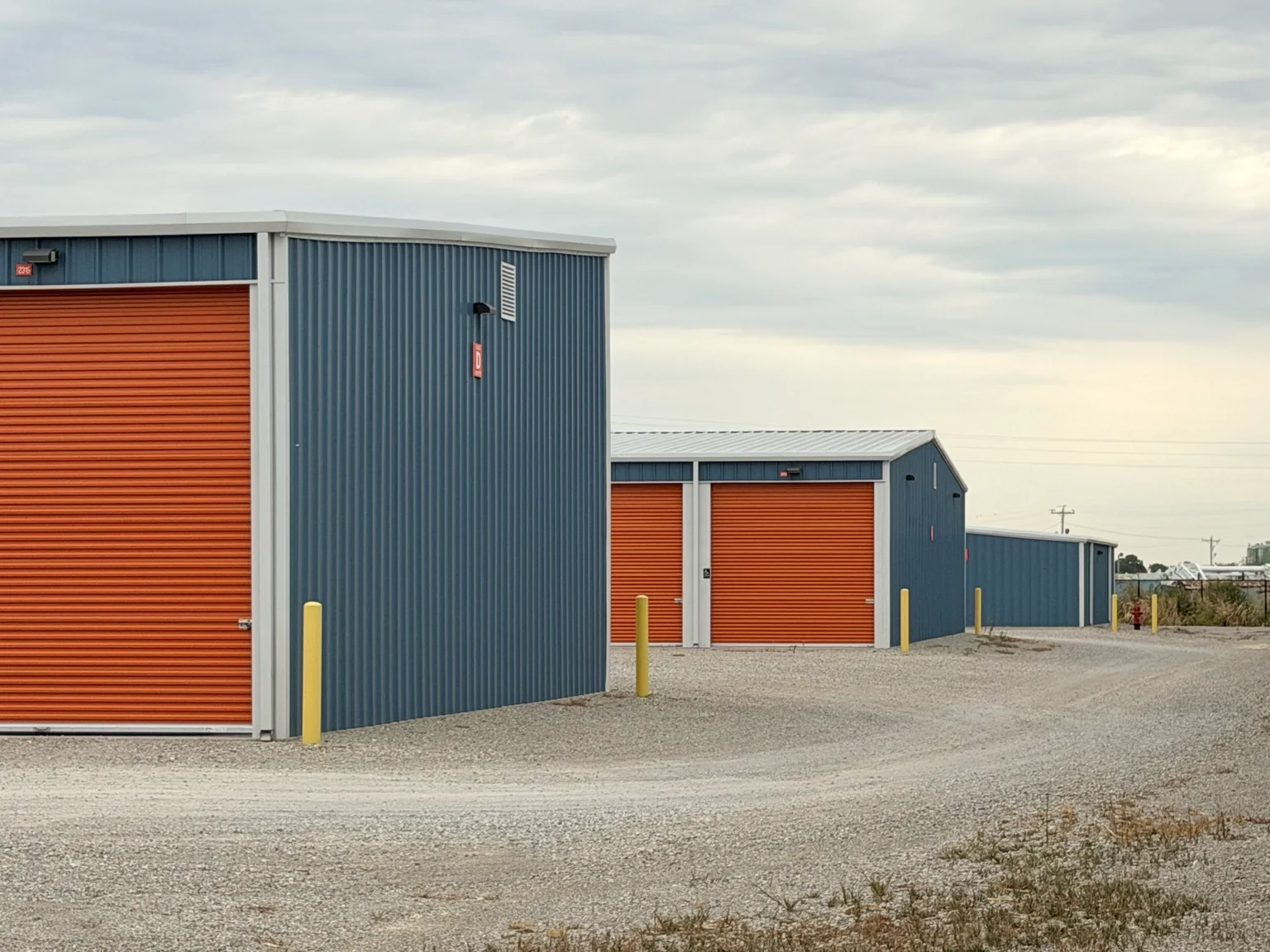 Completed metal storage buildings with orange roll-up doors and yellow bollards